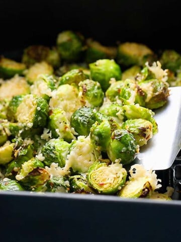 a flat spatula lifting cooked brussels sprouts from an air fryer baset.