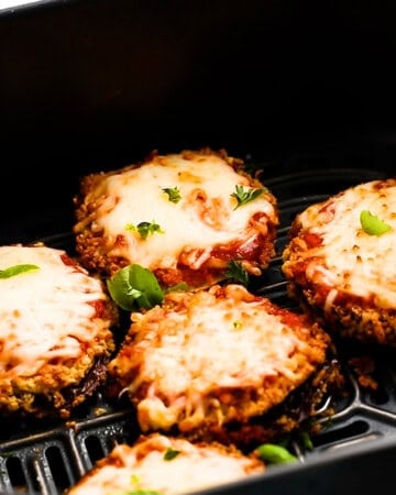 cheesy eggplant slices in an air fryer basket.