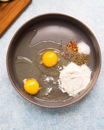 2 eggs, white flour and seasonings in a grey bowl.