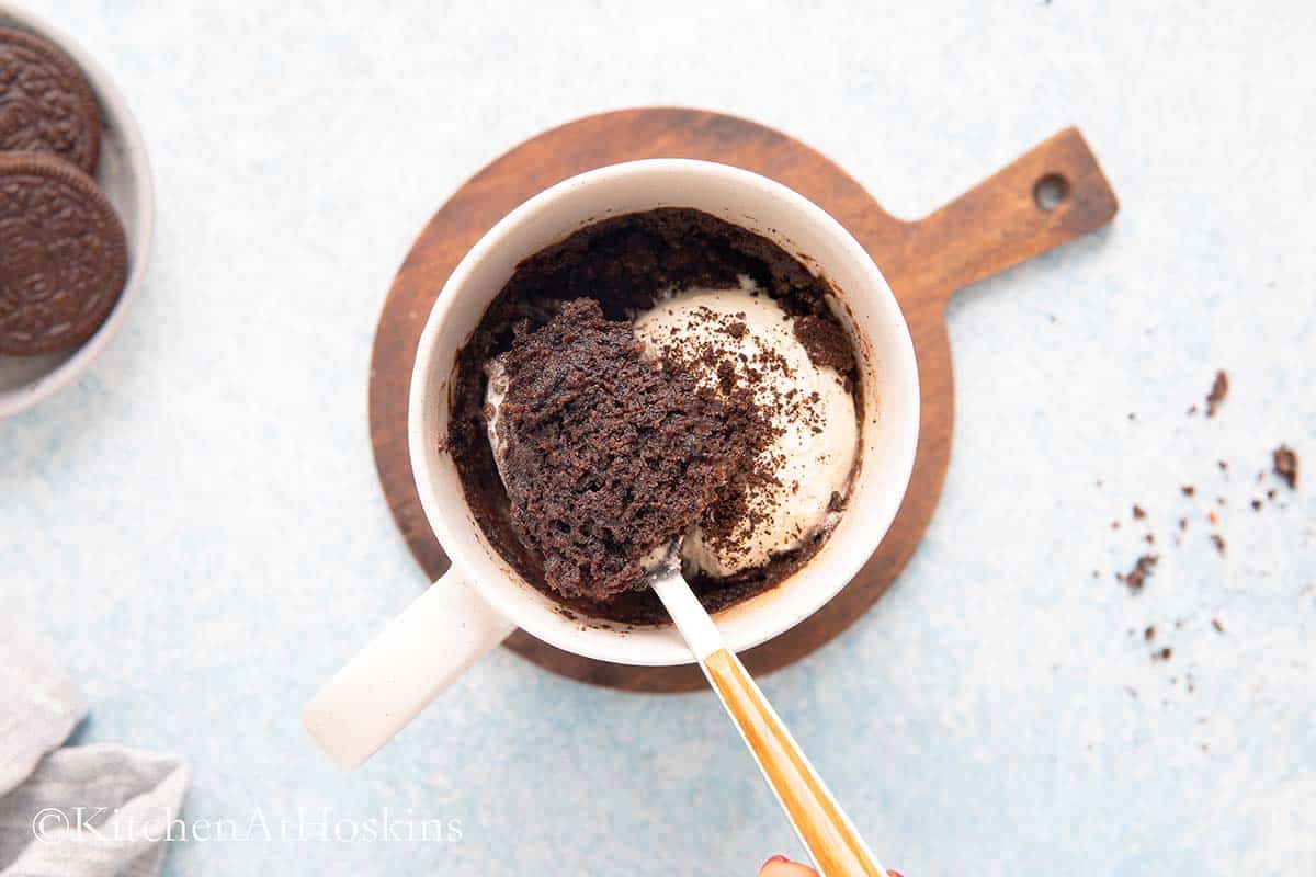 a spoon lifting a bite of oreo cake from a mug.