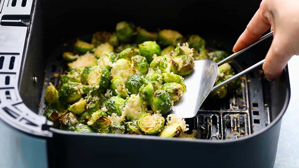 removing roasted brussels sprouts with a flat spatula from the air fryer basket.