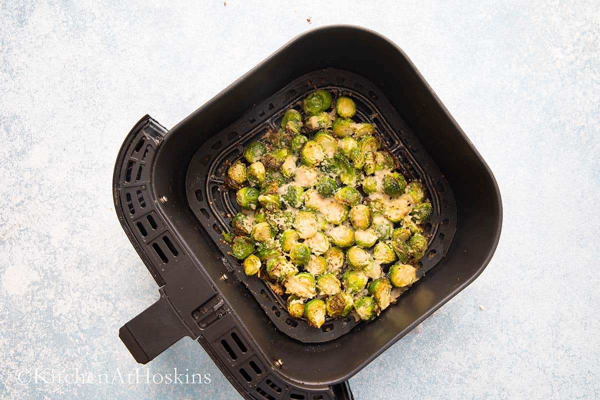 air fryer basket with roasted brussels sprouts topped with parmesan.