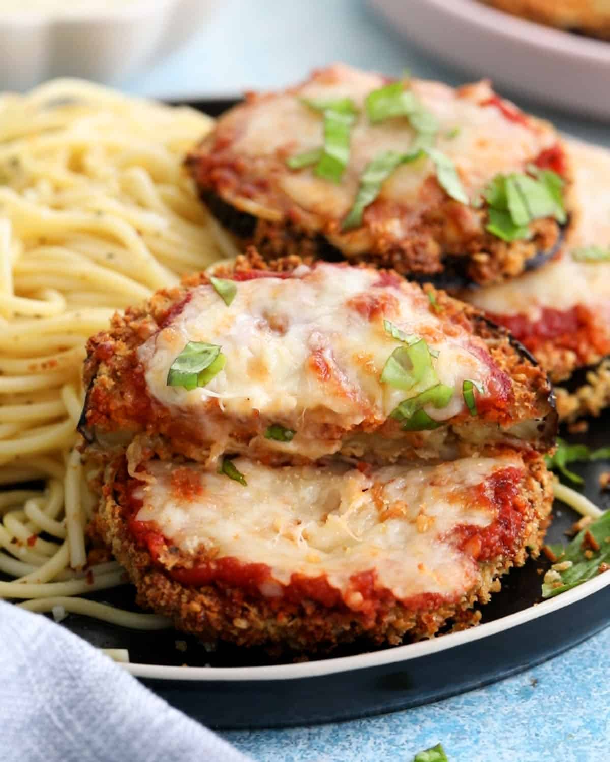 four slices of air fryer eggplant parmesan alongside spaghetti in a black plate.