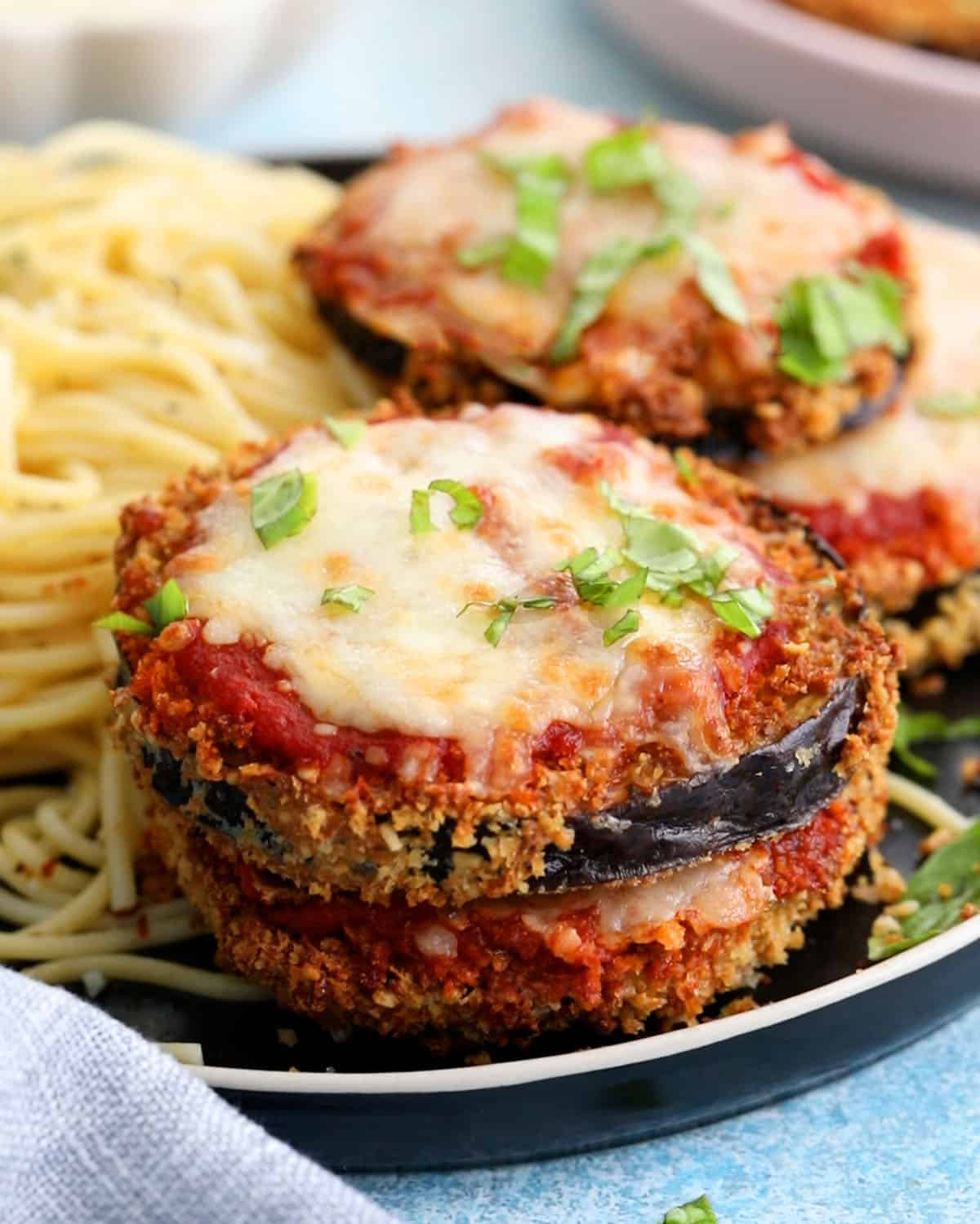 four slices of air fryer eggplant parmesan alongside spaghetti in a black plate.