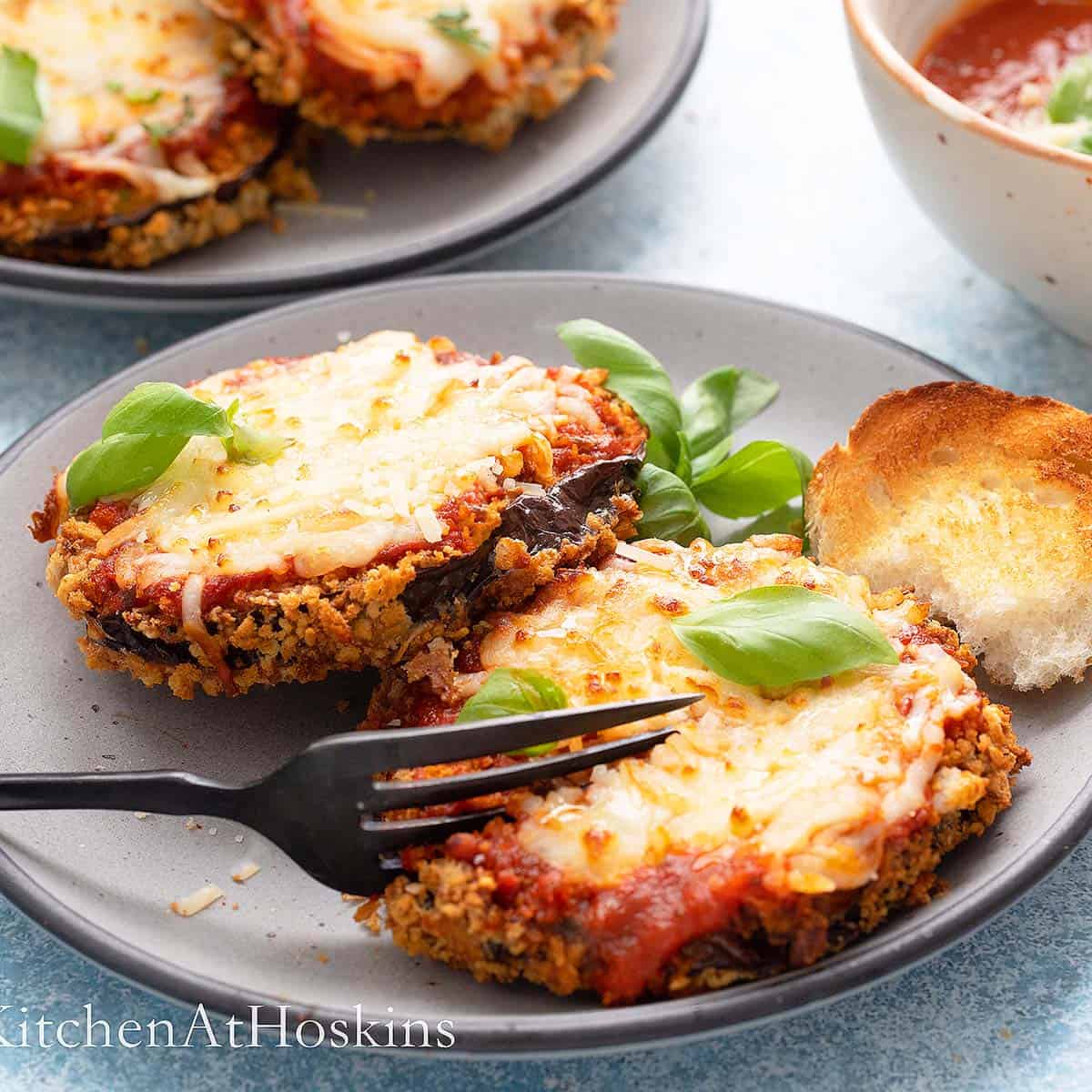 eggplant parmesan on grey plates garnished with basil.