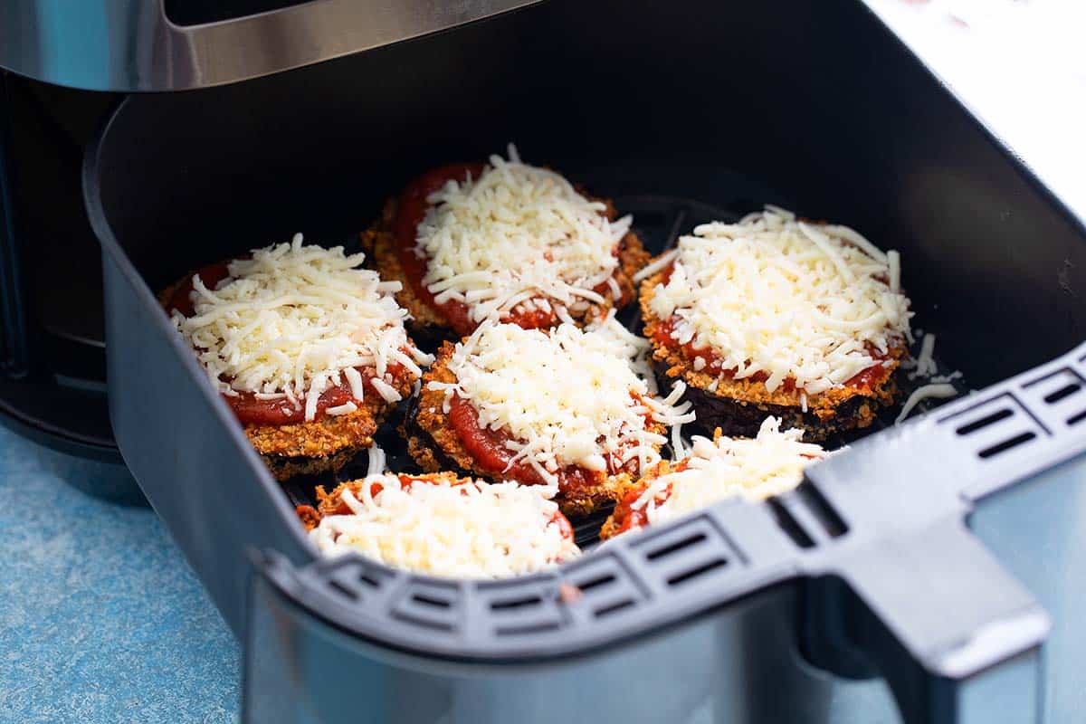 breaded aubergine topped with marinara sauce and cheese in air fryer basket.