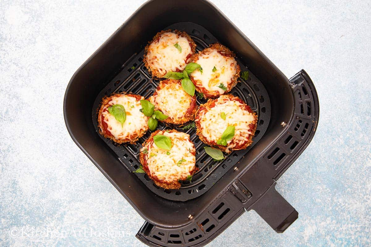 cooked eggplant parm garnished with basil in air fryer basket.