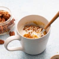 white mug with cooked carrot cake with a spoon.