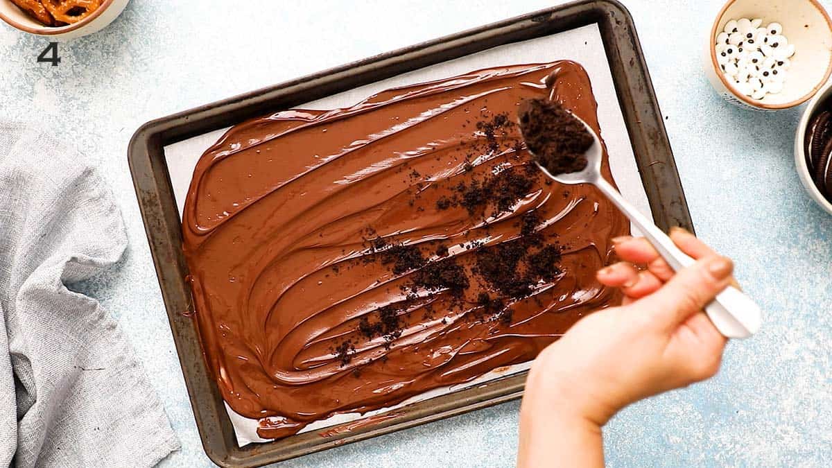 a hand sprinkling crushed oreos using a stainless steel spoon on top of melted chocolate.