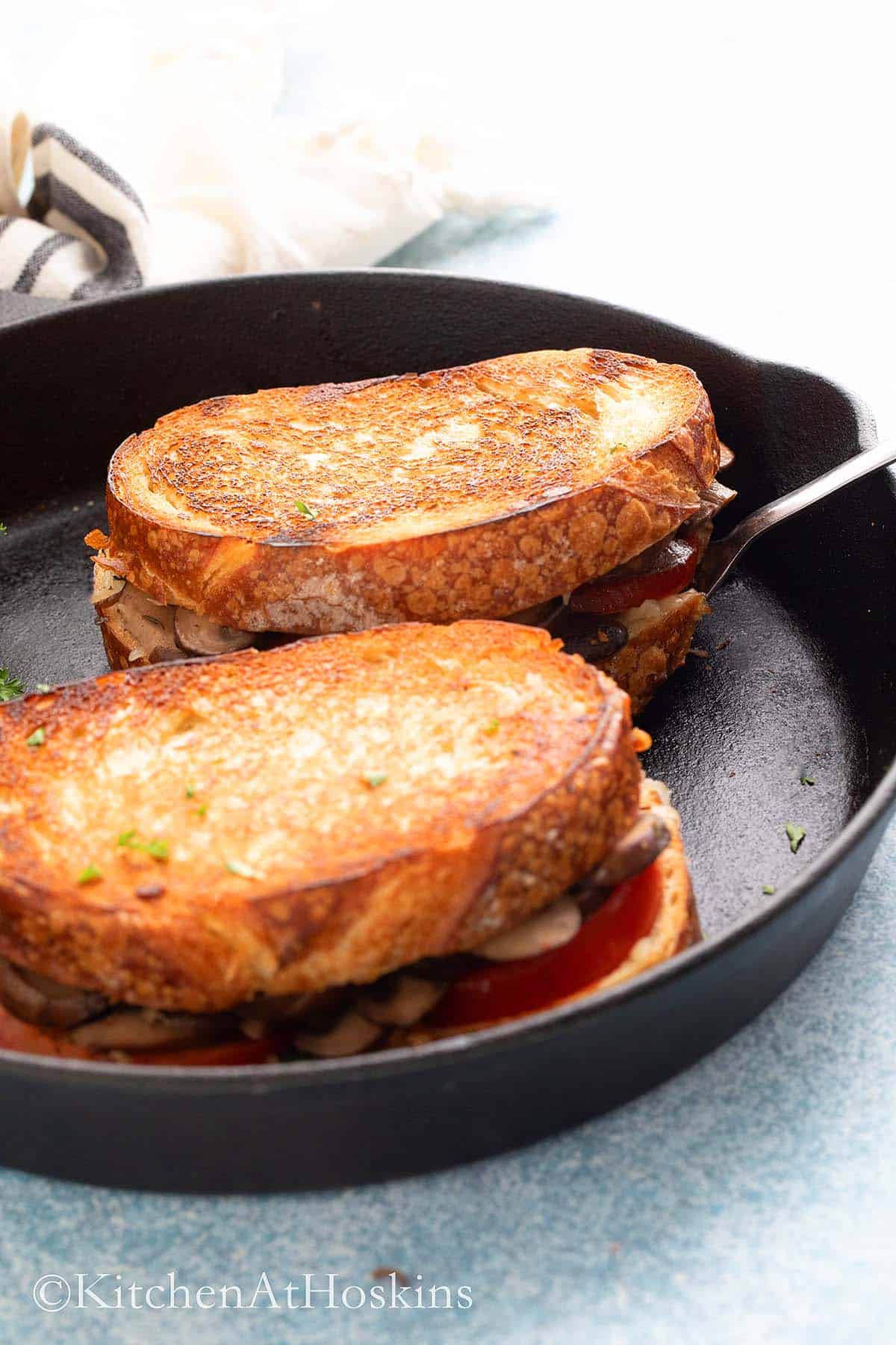 lifting a cooked mushroom grilled cheese from a cast iron skillet.