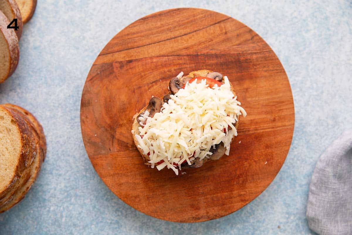 sliced bread topped with white shredded cheese, placed on a round wooden board.