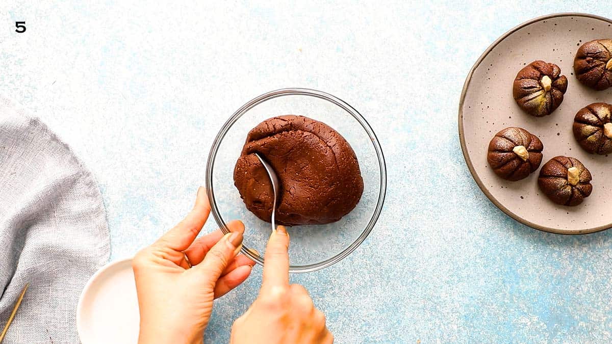 two hands scooping a portion of chocolate dough using a spoon. 