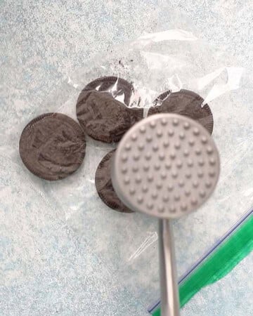 a hand crushing 4 oreo cookies using a meat mallet.