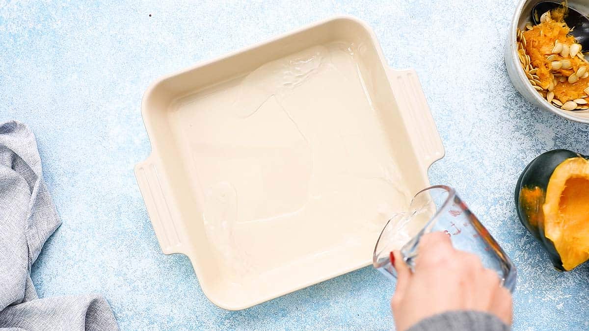 a hand pouring water into a baking dish.