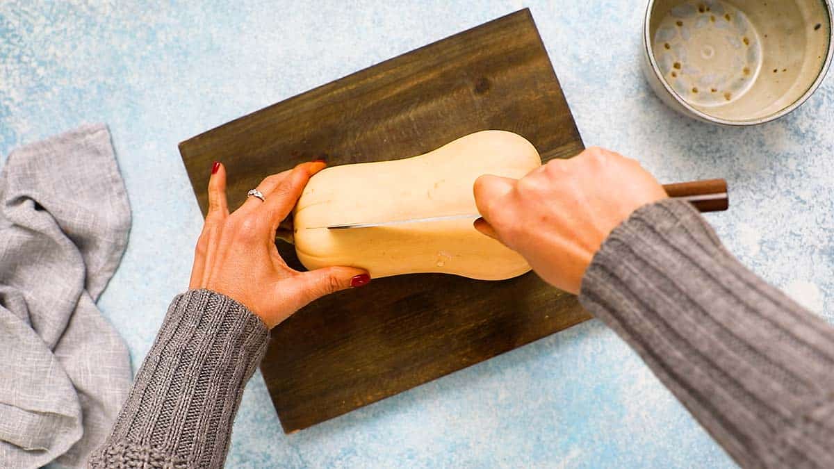 two hands cutting a butternut squash with a knife.