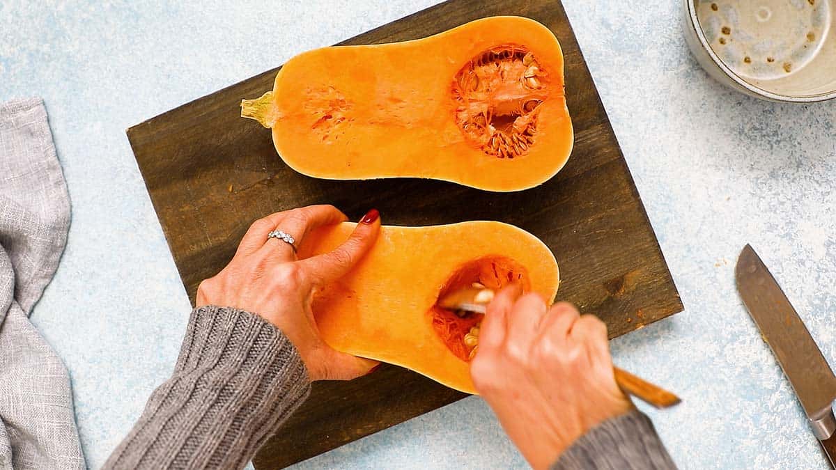 two hands scooping out the seeds from a squash with a spoon.