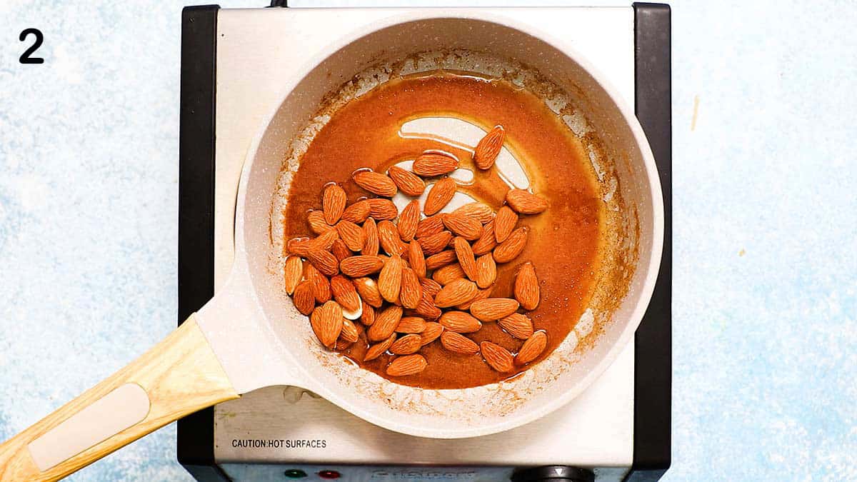 small white skillet on a stovetop with almonds and caramel syrup.