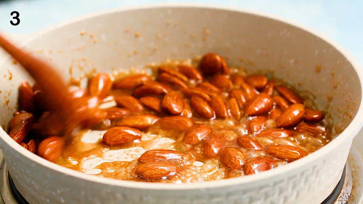 almonds cooking in syrup in a small white skillet.