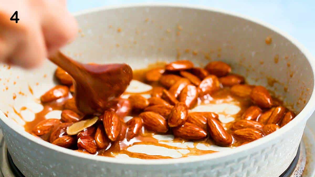 a hand stirring almond in caramel syrup in a small white skillet.
