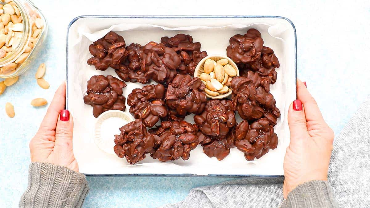 2 hands holding a tray filled with chocolate peanut clusters.