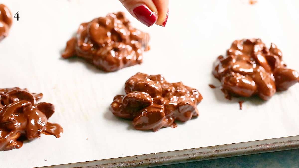 a hand sprinkling salt on mounds of chocolate peanut clusters.