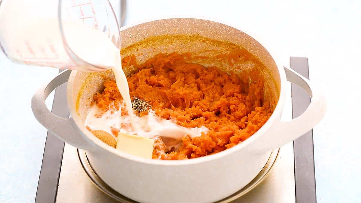 Pouring milk into a pot of mashed sweet potatoes.
