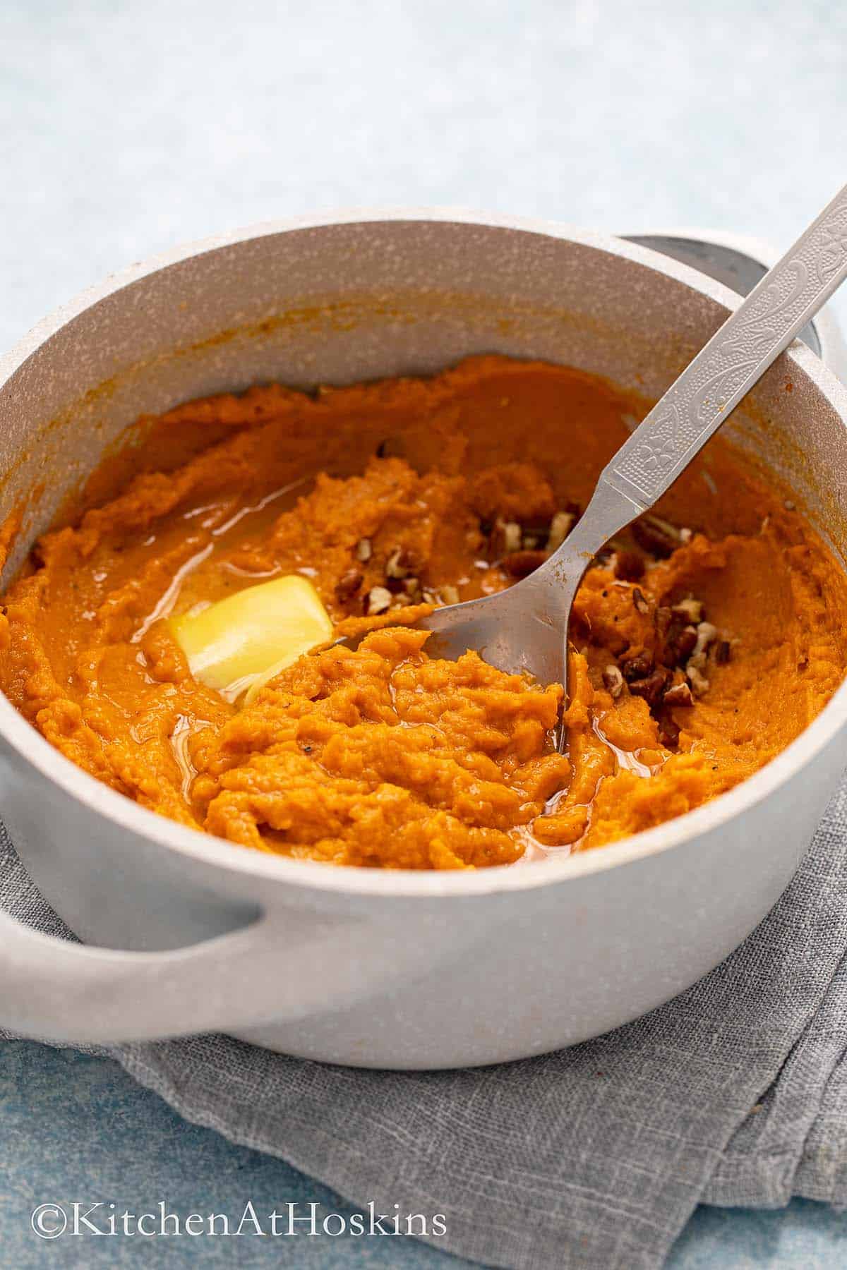 a pot with mashed sweet potatoes along a spoon topped with butter.