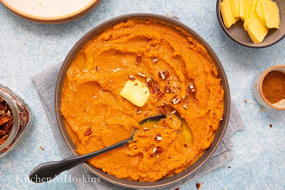 round platter filled with mashed sweet potatoes topped with butter and pecans.