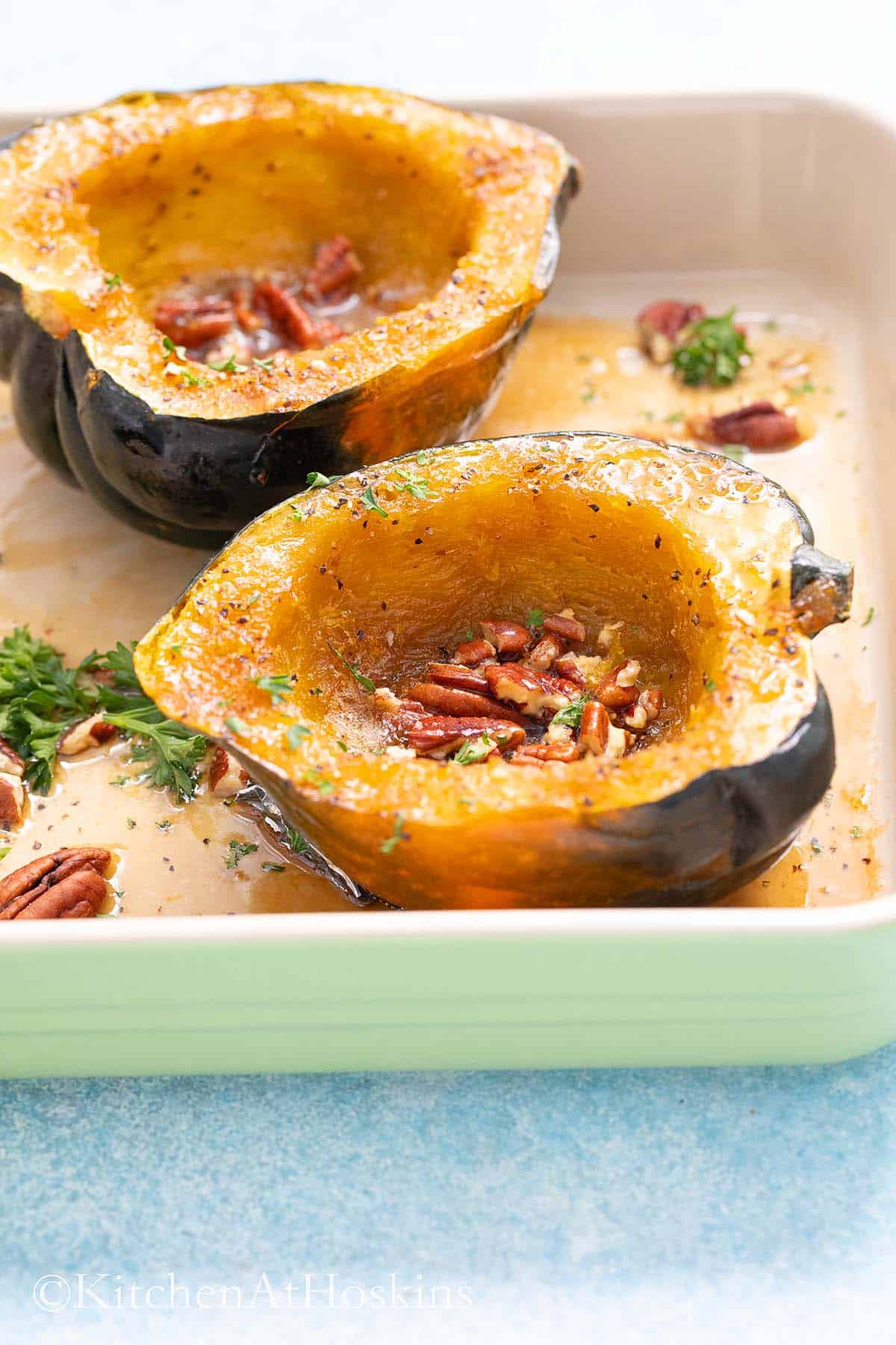 microwaved acorn squash halves with pecans in a baking dish garnished with parsley.