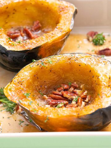 cooked acorn squash halves in a baking dish with pecans.