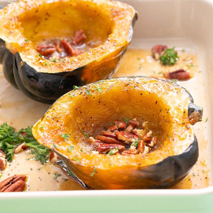 cooked acorn squash halves in a baking dish with pecans.