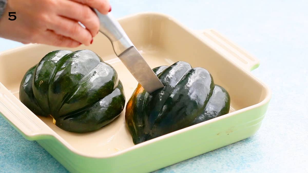 a hand inserting a knife into a cooked acorn squash half.