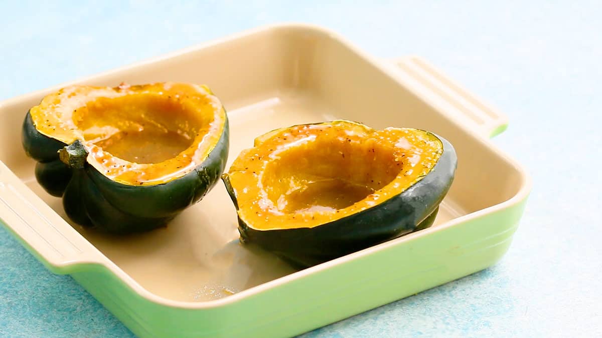 two cooked acorn squash halves in a green square ceramic baking dish.