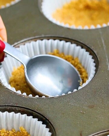 a hand pressing graham cracker crust using a tablespoon measure.