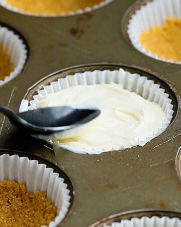 a hand spreading white cheesecake filling in a muffin pan.