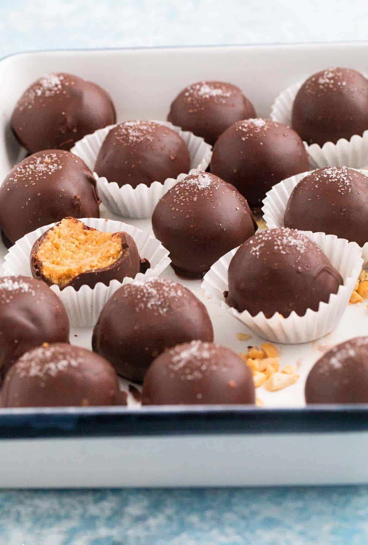 chocolate coated peanut butter balls topped with salt in a white tray.