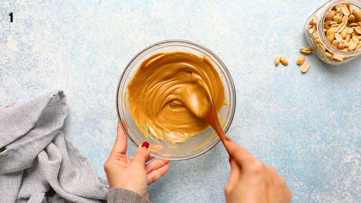 two hands stirring melted peanut butter mixture in a small glass bowl. 