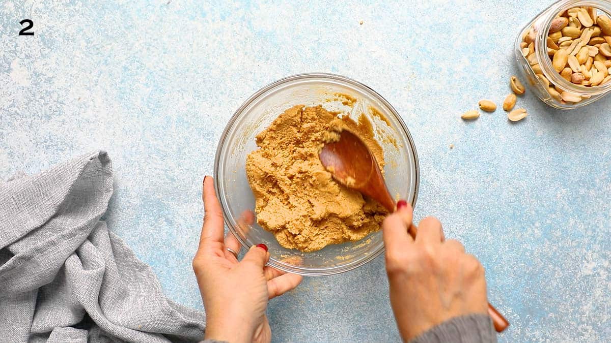 two hands mixing peanut butter dough in a glass bowl.