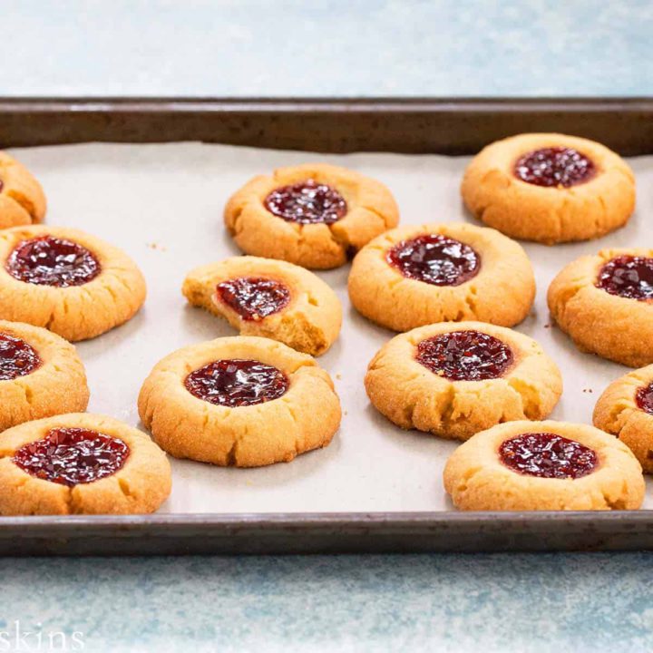 raspberry thumbprint cookies on a parchment lined baking sheet.