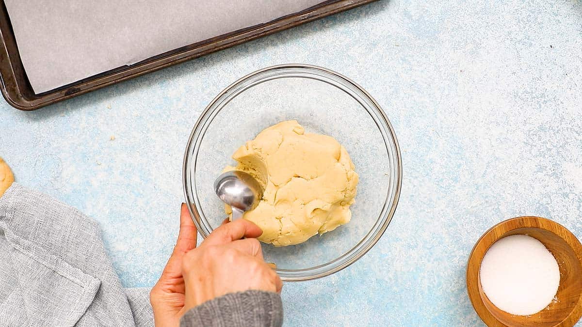 a hand scooping dough with a tablespoon.