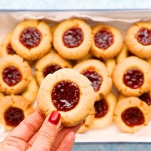 a hand holding one raspberry thumbprint cookie.