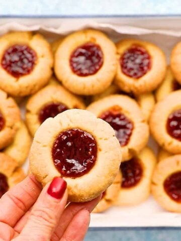 a hand holding one raspberry thumbprint cookie.