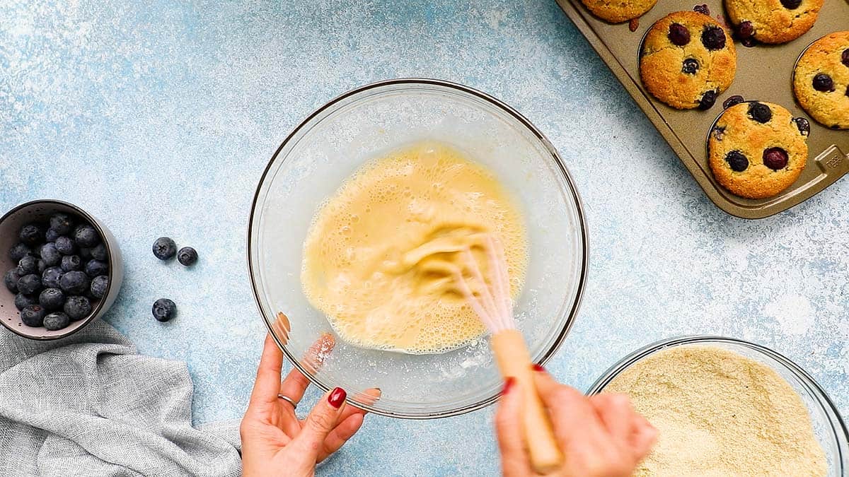 two hands whisking wet ingredients in a glass bowl.
