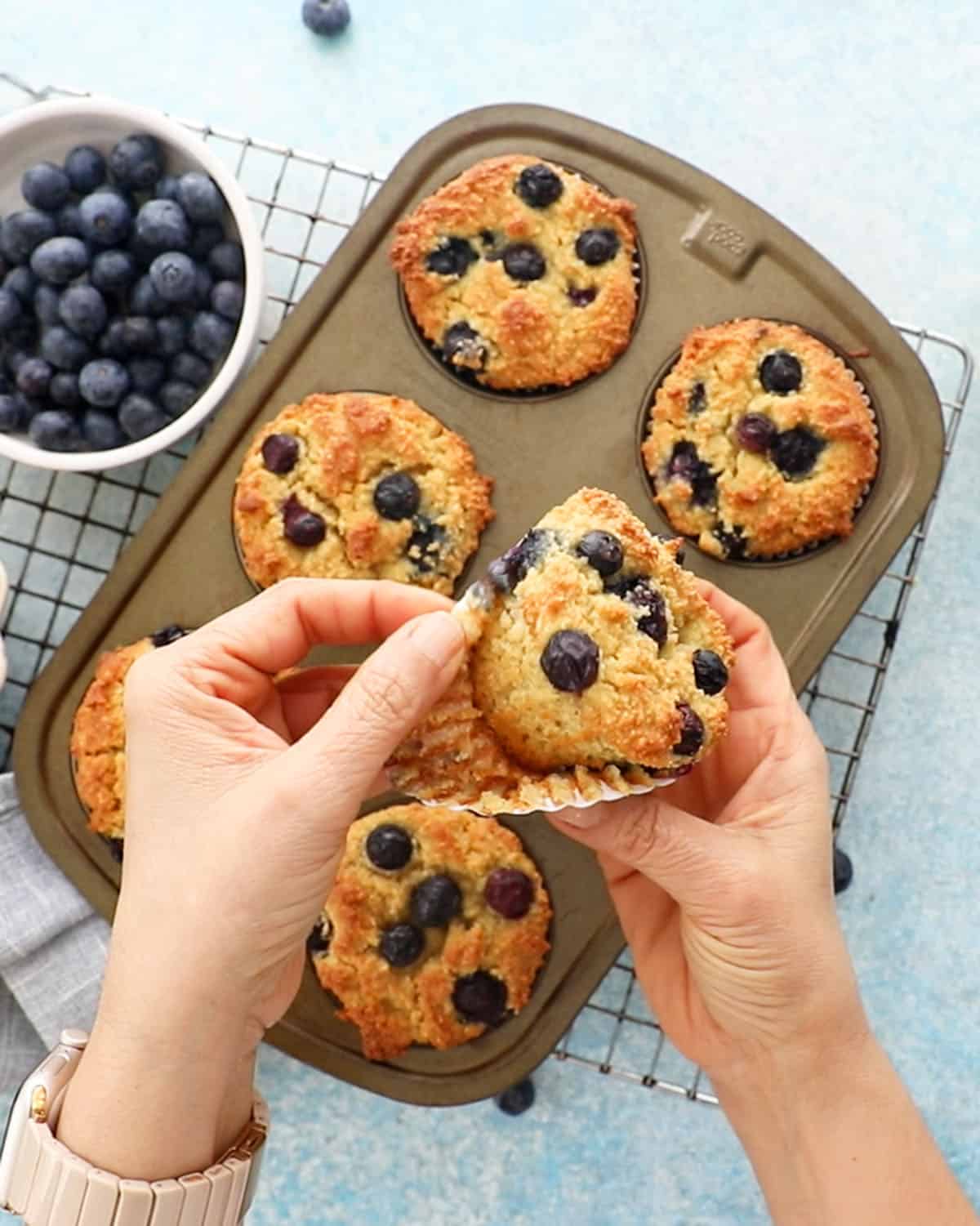 two hands holding one almond flour blueberry muffin.