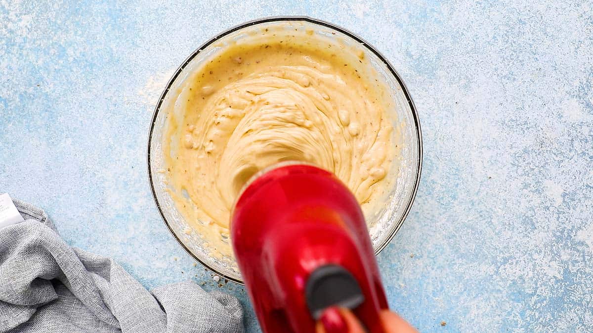 a electric beater mixing banana cake batter in a glass bowl.