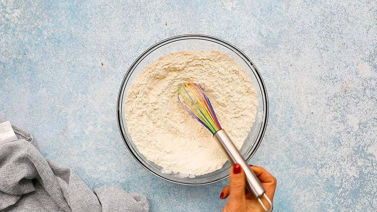 a hand whisking flour in a glass bowl.