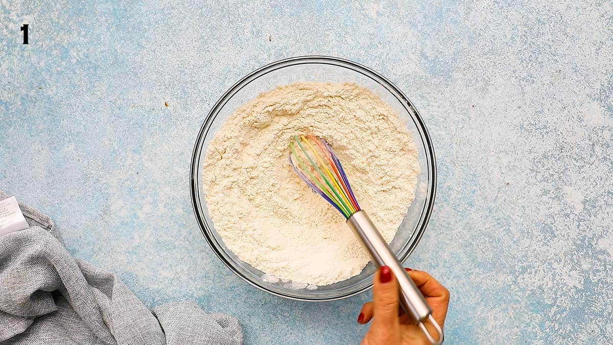 a hand mixing flour in a glass bowl using a whisk.