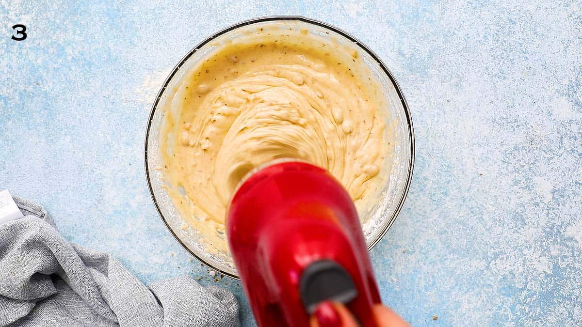 beating cake batter in glass bowl with red electric beater.