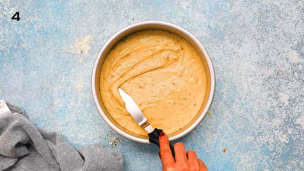 a hand spreading cake batter in round  aluminium pan with offset spatula.