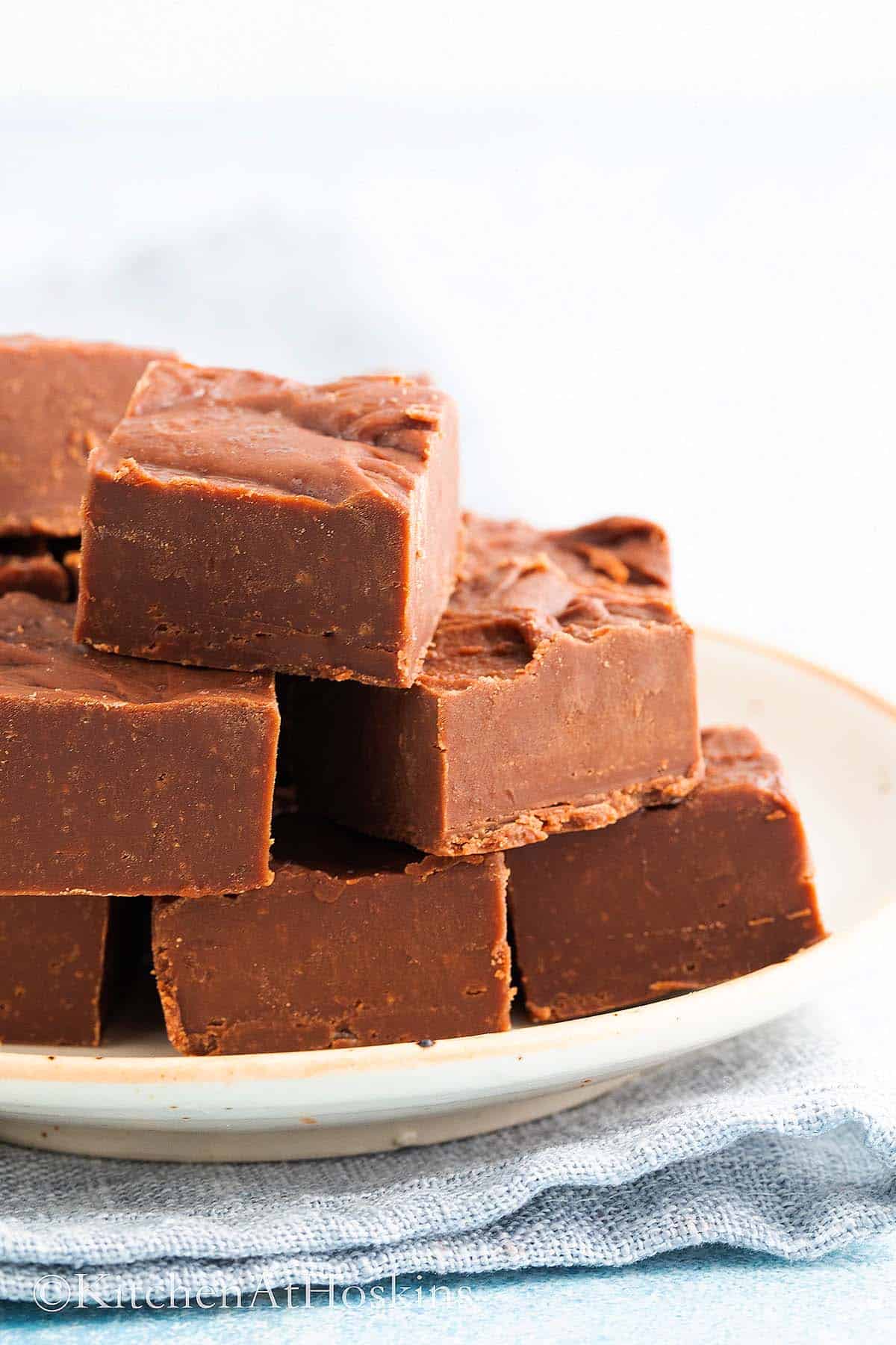 peanut butter fudge squares stacked on a white plate.